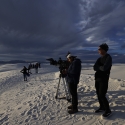 a film stands on sand dunes with camera equipment 
