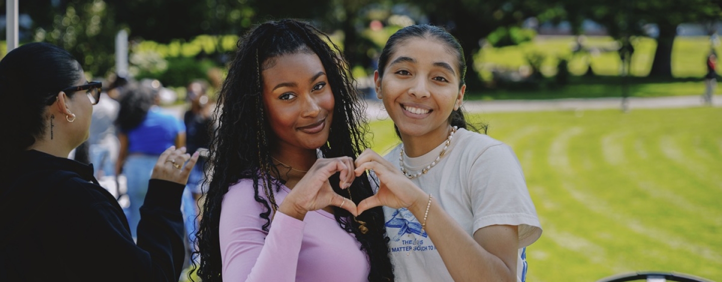 Two female students make a heart shape with their hands