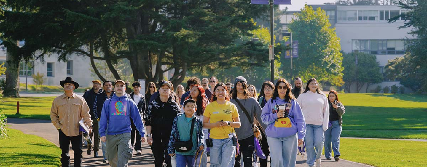A student tour guide leads future SFSU students and families on a walk through the Quad on a sunny day 