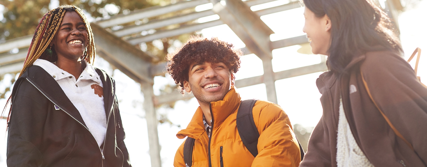 Three smiling students hanging out with each other in a group.