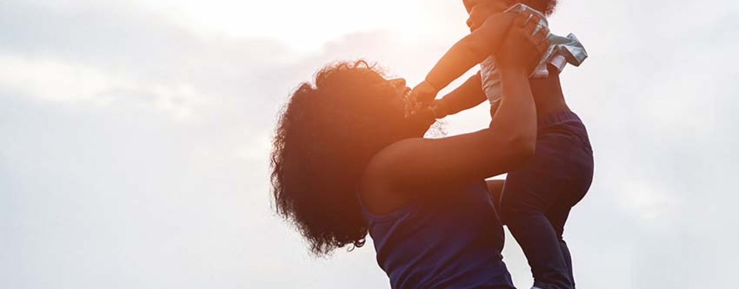 Mom holding up her toddler against a sunset