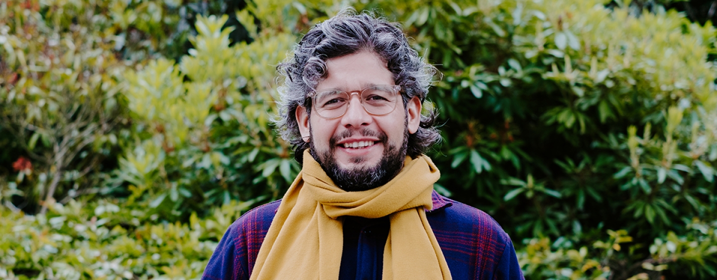 Personal smiling against green foliage in the background.
