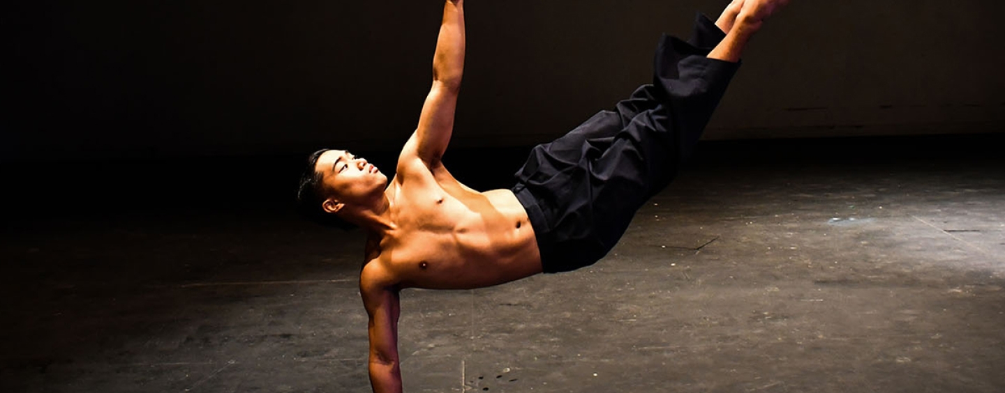 Johan Casal balances himself on his right hand while lifting his right arm and legs in the air while dancing in a studio