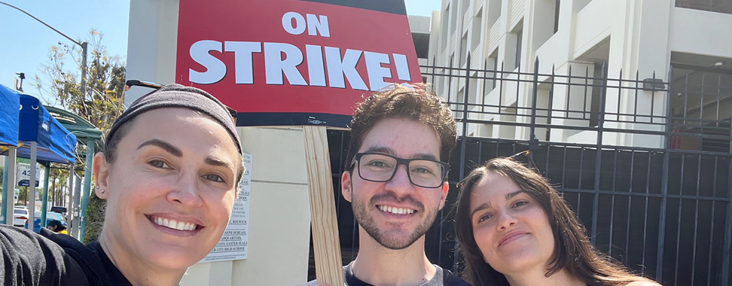 From left: Lecturer Marion Dayre takes a selfie with alumni Armando Jimenez and Barbara Burgues on the picket line with a sign reading Writers Guild of America on Strike!