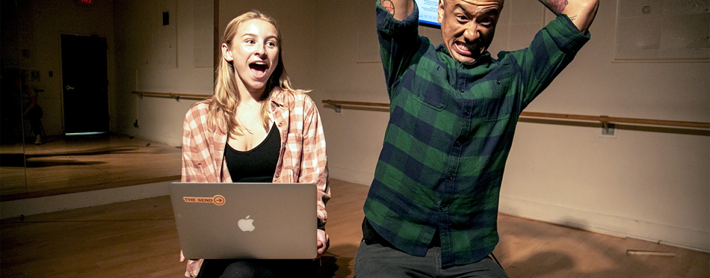 One actor holds his laptop over his head about to slam it on the ground while an actress watches while seated with her laptop on her lap