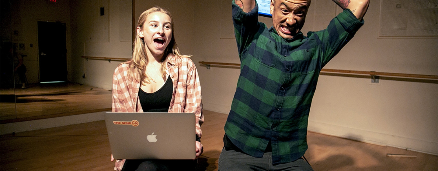  One actor holds his laptop over his head about to slam it on the ground while an actress watches while seated with her laptop on her lap 