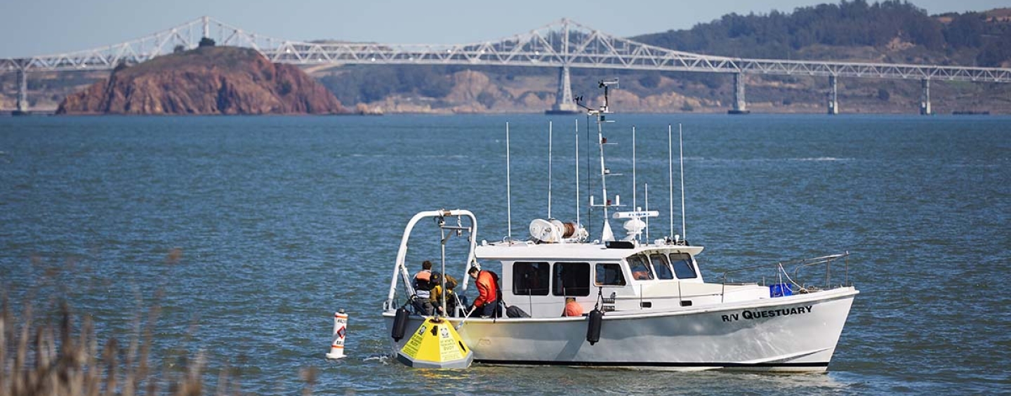 EOS researchers on a boat unloading a yellow buoy into the water