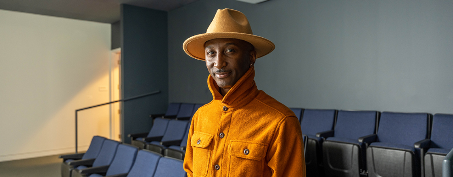 Artel Great stands in a screening room wearing an orange hat and orange collared shirt