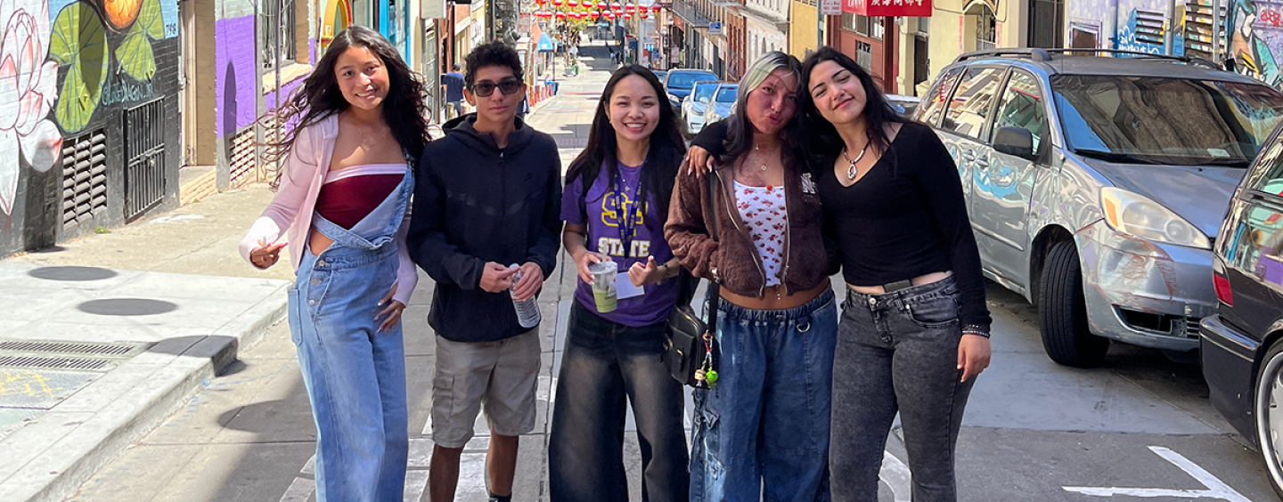 Five students pose for a photo while standing in a street in the Chinatown neighborhood of San Francisco on a sunny day