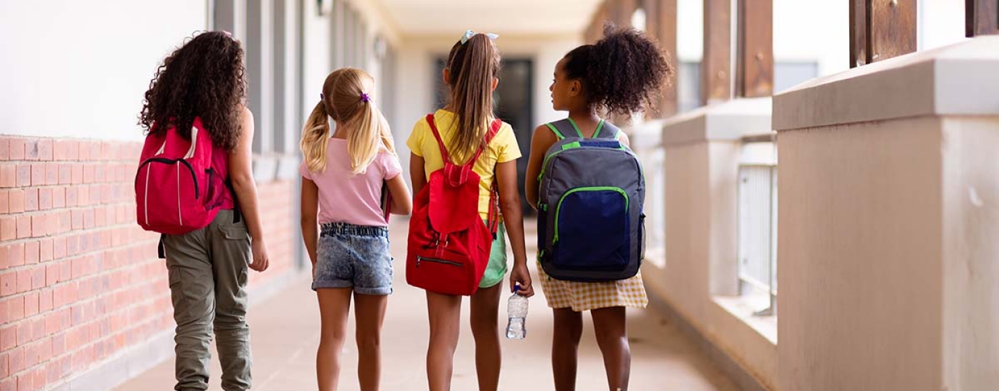 Four girls wearing backpacks walking to school