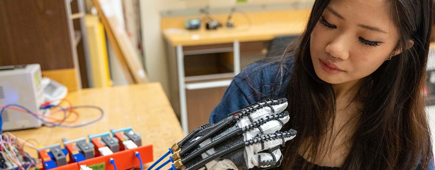 Lauren Gan wears and looks at robotic hand project