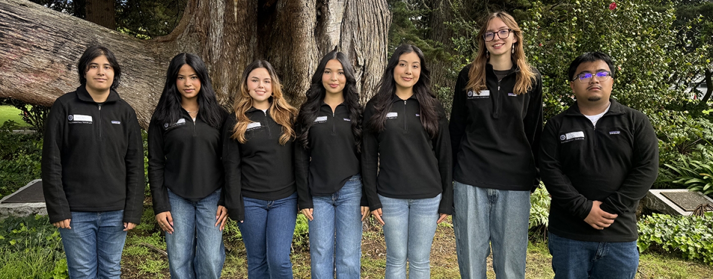 A group of students standing in a line posing for the camera with trees in the background.