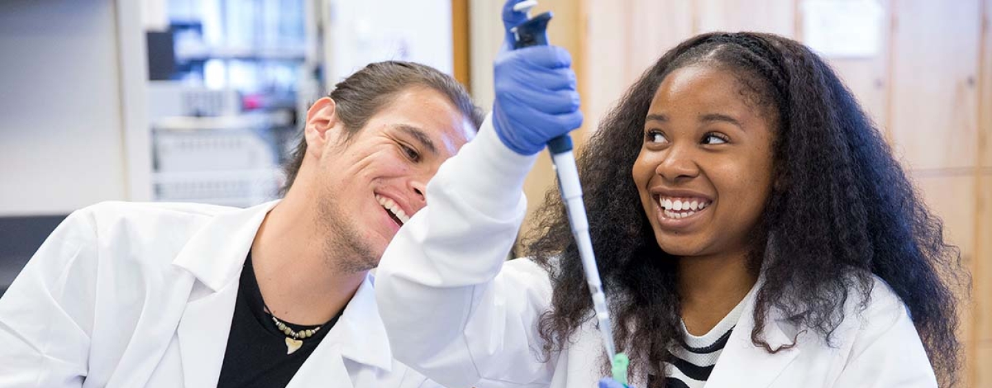 Two smiling people pipetting for a molecular biology experiment