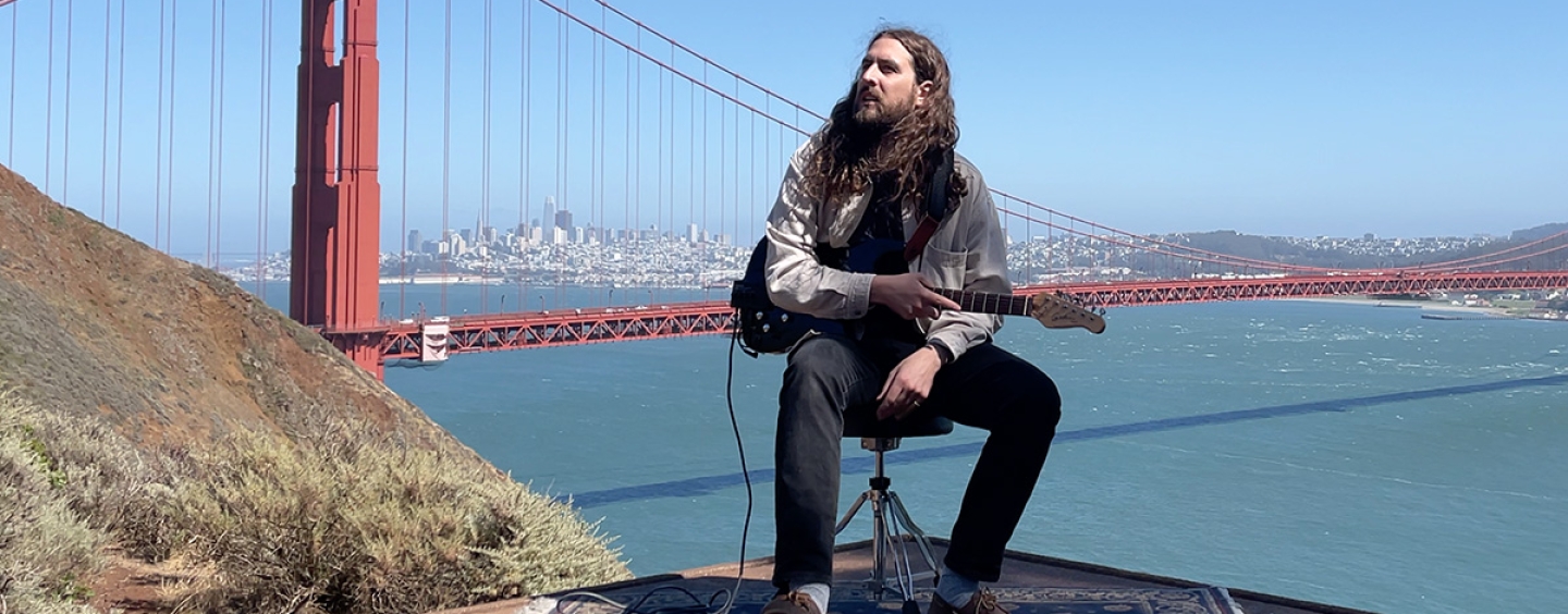 Nate Mercereau seated outdoors in the Marin Headlands holding a guitar