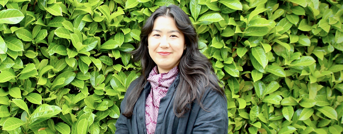 A woman smiling with green foliage in the background.
