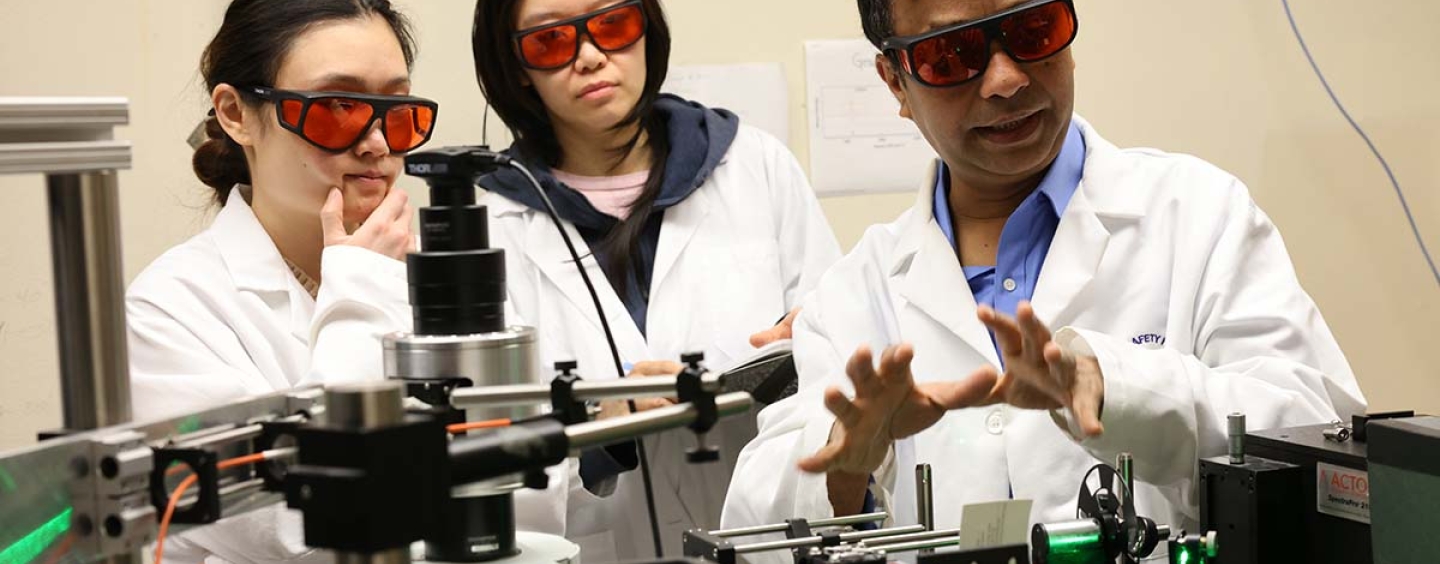 Two female students watching Professor AKM Newaz talk about a laser in the lab