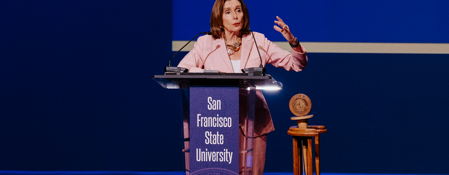 Nancy Pelosi gestures with her left hand while speaking at a lectern with the text San Francisco State University