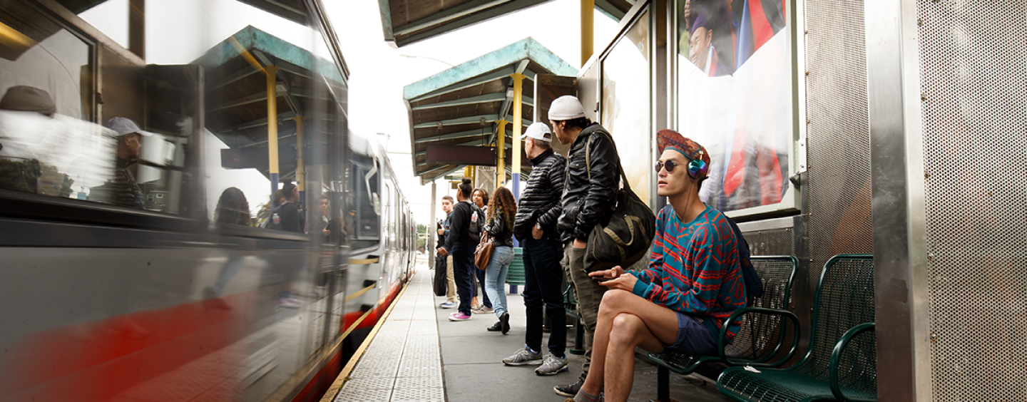 People sit at the SF State/Parkmerced Muni station while a train is stopped