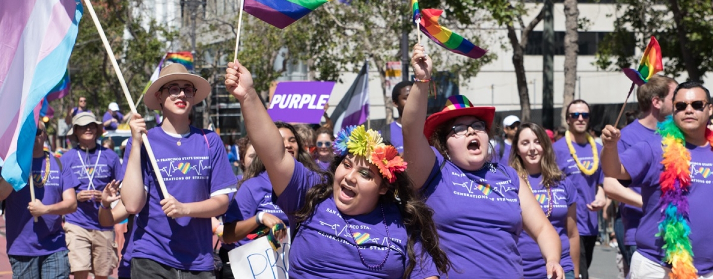Students in purple wave rainbow flags in a Pride parade