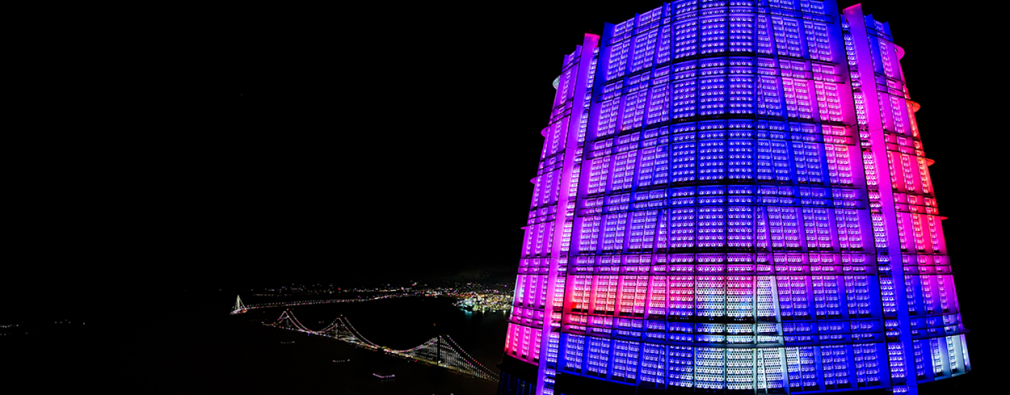 A drone photo of the top of the Salesforce Tower in San Francisco showing colorful SFSU student artwork with the Bay Bridge visible in the background