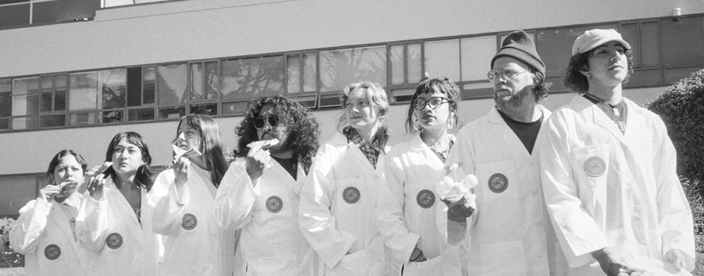 Black and white photo of seven SFSU students in lab coats standing on the Quad