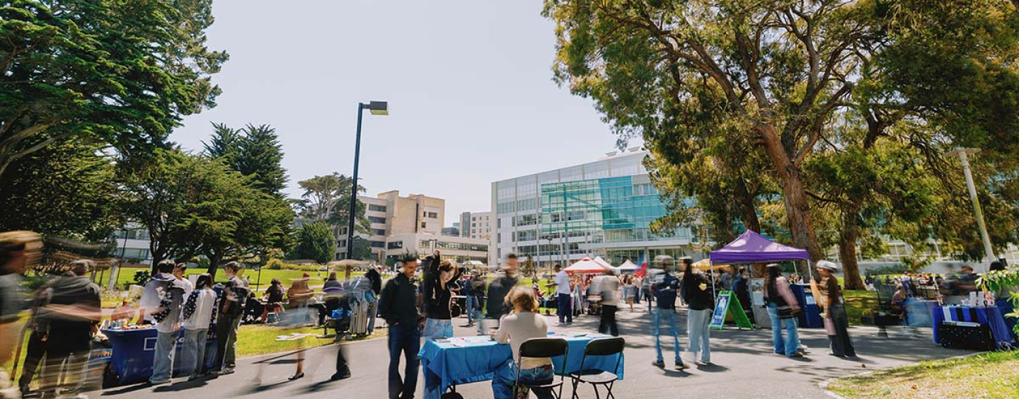People walk across the Quad among tables on a sunny day