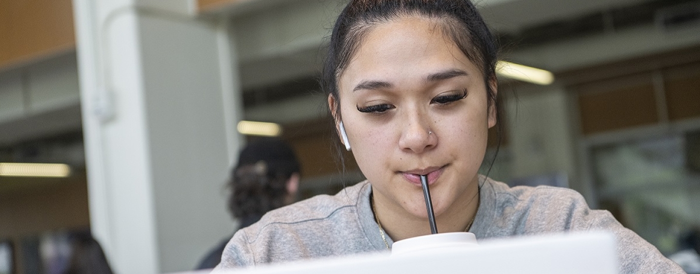 A woman sucks on a straw while looking at a laptop