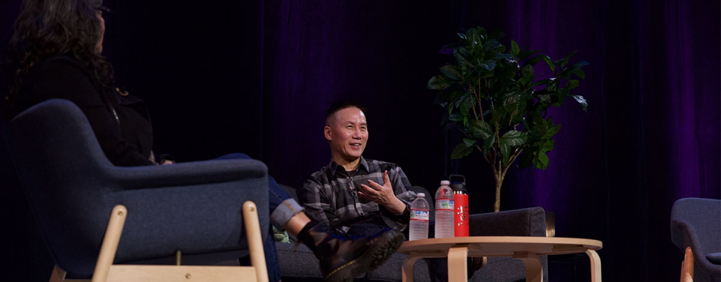 Actor BD Wong sits in a chair on a stage across from a woman