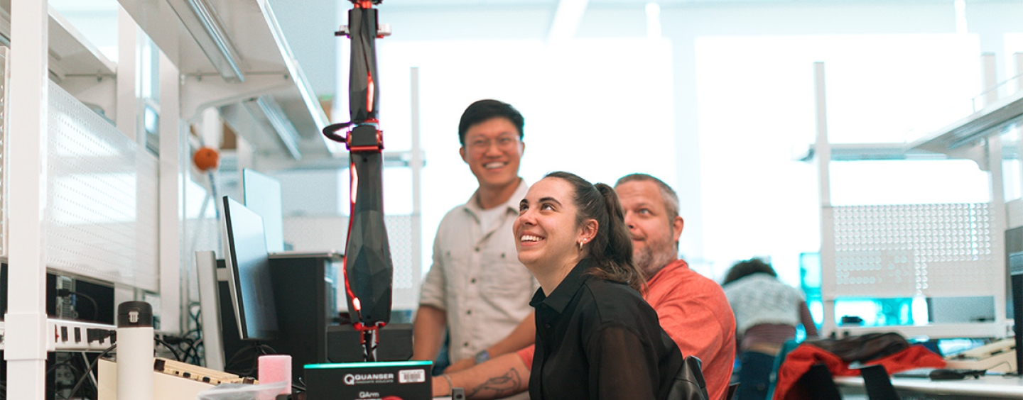 three students looking at a fully extended robotic arm