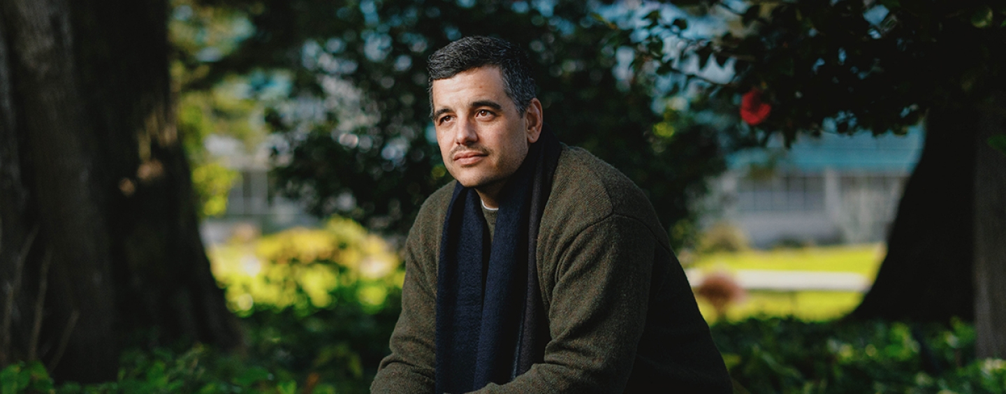 Man in olive green jacket and jeans sitting on a concrete bench.
