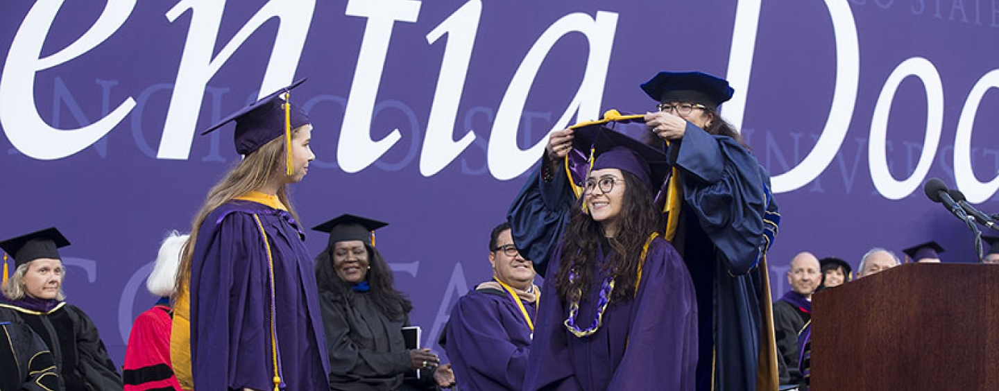 The Dean of the College of Science & Engineering places an honorary hood over over a student dressed in regalia 