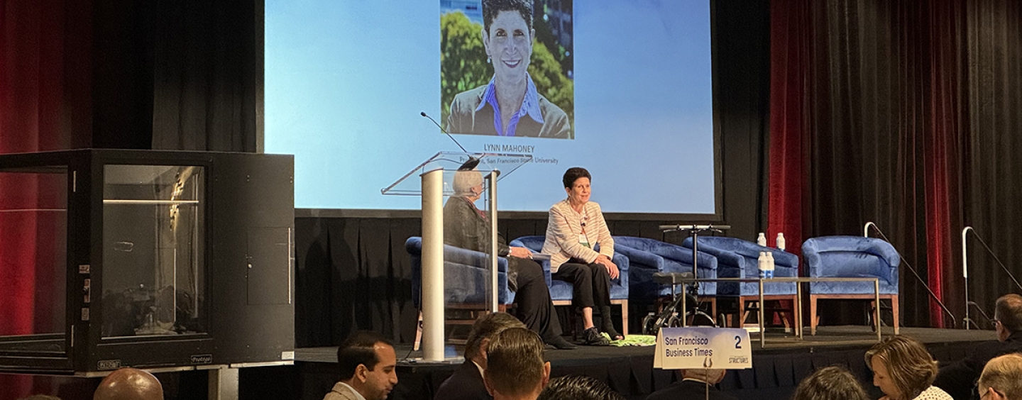 Two people sitting on a stage speaking to a crowd.