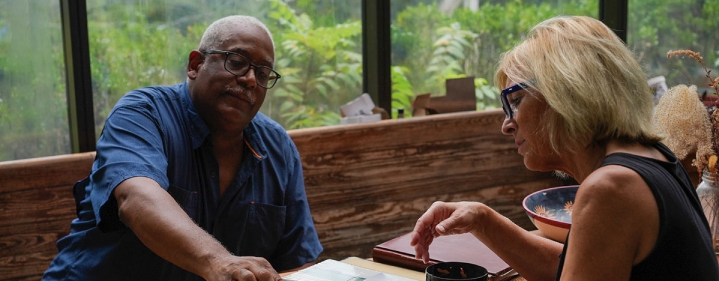 Maggie sits at a table with a man as they look at a photo album