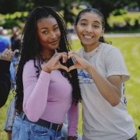 Two female students make a heart shape with their hands