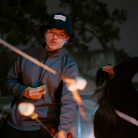 At an evening bonfire, a person lights a marshmallow on a stick while others watch 