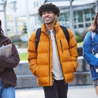 Three students walking in a line on a university campus while they are smiling.