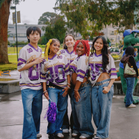 Five people wearing SF State Gators football jerseys and blue jeans stand on Malcolm X Plaza on an overcast and rainy day