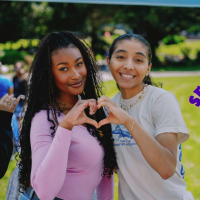 Two students make a heart shape with their hands with the Gator Giving Day logo pasted in the right side of the photo