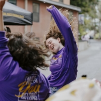 Two students standing outside raise their arms as they dance and cheer