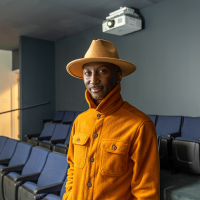 Artel Great stands in a screening room wearing an orange hat and orange collared shirt