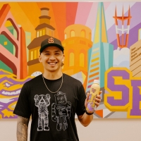 Jordan Herren stands in from of painting that he made that hands in SF State's administration building while holding a water bottle he illustrated