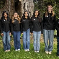 A group of students standing in a line posing for the camera with trees in the background.
