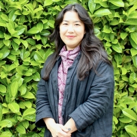 A woman smiling with green foliage in the background.