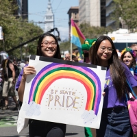 Two students marching in a parade stand in front of a hand-made sign saying "SF State Pride"