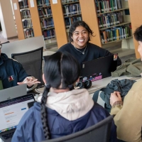Four students sitting around a table in the library, chatting and using laptops