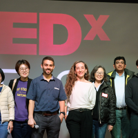 Nine students, faculty and administrators stand on stage in front of a screen projecting the TEDx logo