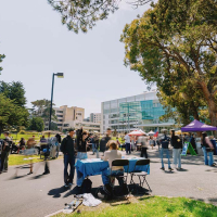 People walk across the Quad among tables on a sunny day