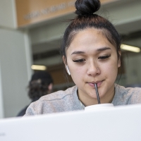 A woman sucks on a straw while looking at a laptop