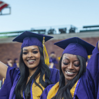 two people with long hair dressed in purple and gold reglia raise their arms in celebration