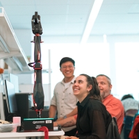 three students looking at a fully extended robotic arm
